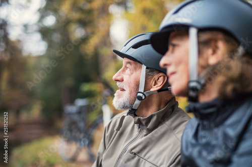 A senior couple with bicycle helmet standing outdoors in park in autumn.
