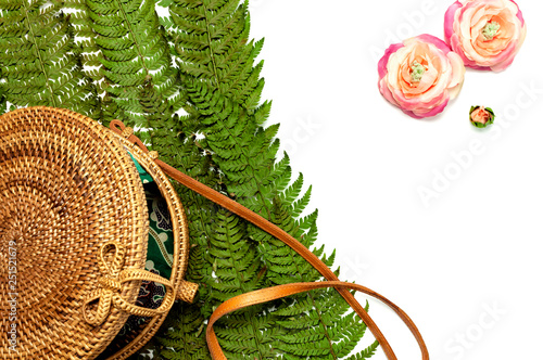 Fashionable handmade natural organic rattan bag and green fern leaves, pink flower isolated on white background. Ladies bag, Stylish rattan bag. Flat lay, top view, copy space. Ecobags from Bali. photo