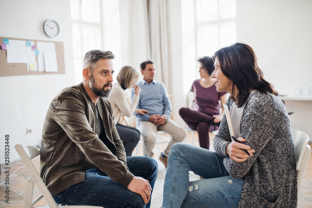 Senior counselor with clipboard talking to a man during group therapy. Senior counselor with clipboard talking to a man during group therapy.