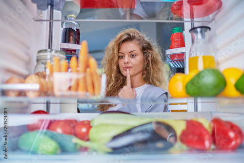 Woman standing in front of fridge full of groceries and taking juice. Picture taken from inside of fridge.