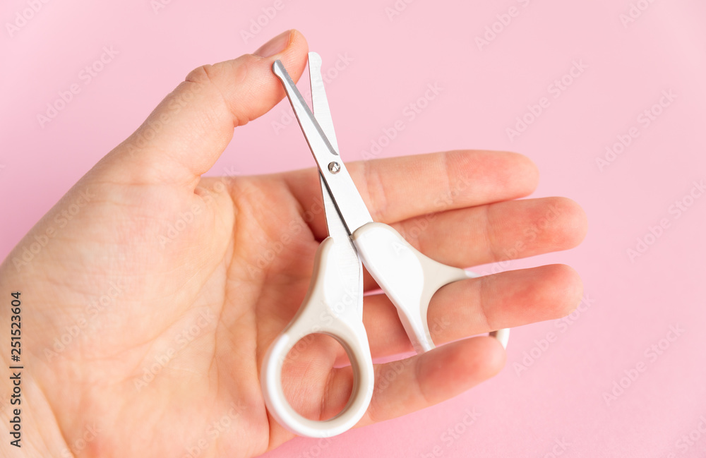 Female hand holding of little opened scissor for baby care. Close up of metal and plastic scissors for child care. Pink studio background. Concept of cutting baby nails. Female hand holding of little opened scissor for baby care. Close up of metal and plastic scissors for child care. Pink studio background. Concept of cutting baby nails.