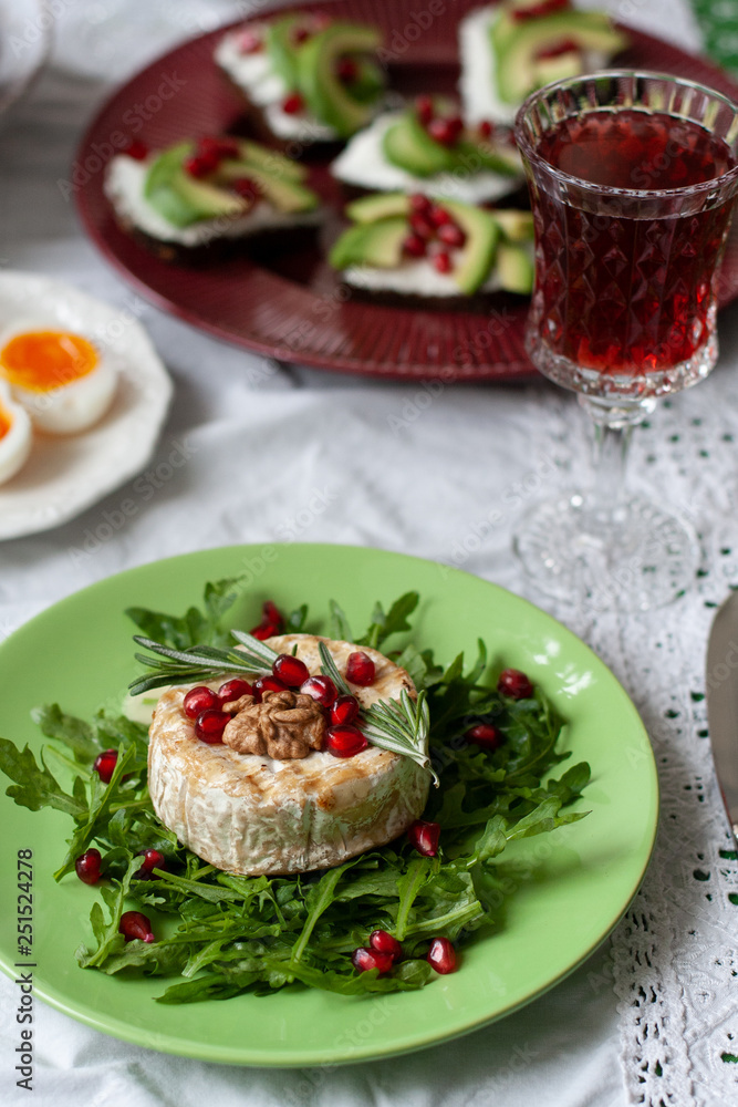 Healthy nutritious lunch or dinner for two: grilled camembert with grains of pomegranate, a branch of rosemary and nuts on a cushion of arugula. 