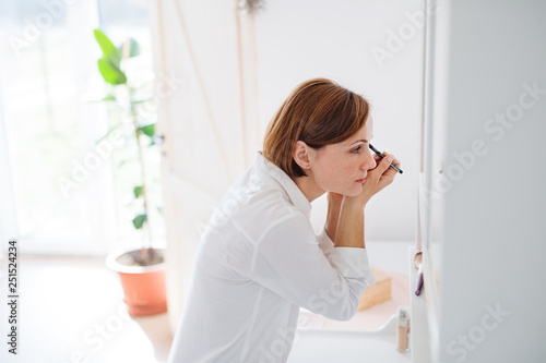 A young woman putting on a make-up in the morning in a bathroom.