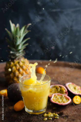 Glasses of juice with tropical fruits on the table on a dark background.