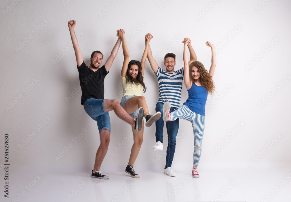 Portrait of joyful young group of friends standing in a studio, lifting legs. Portrait of joyful young group of friends standing in a studio, lifting legs.