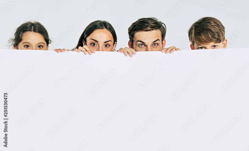 Beautiful smiling family in white T-shirts hold in hands the big blank banner and looking on camera Beautiful smiling family in white T-shirts hold in hands the big blank banner and looking on camera