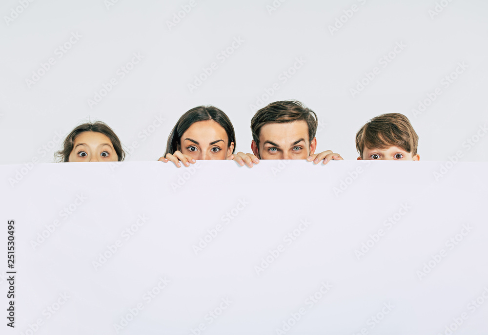 Beautiful smiling family in white T-shirts hold in hands the big blank banner and looking on camera Beautiful smiling family in white T-shirts hold in hands the big blank banner and looking on camera