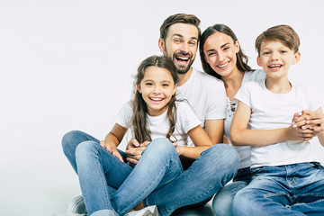Relationship concept. Beautiful and happy smiling young family in white T-shirts are hugging and have a fun time together while sitting on the floor and looking on camera.