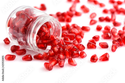 Pomegranate seeds placed in glass jar with scattered seeds on white background