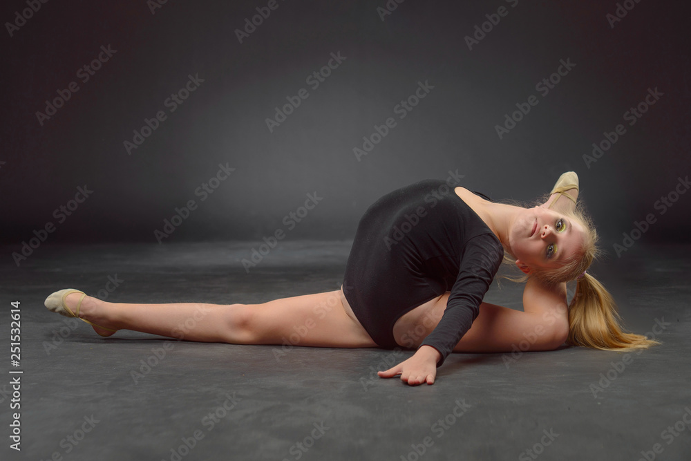 Obraz premium beautiful white caucasian girl gymnast doing gymnastic exercise for flexibility and stretching on black background.