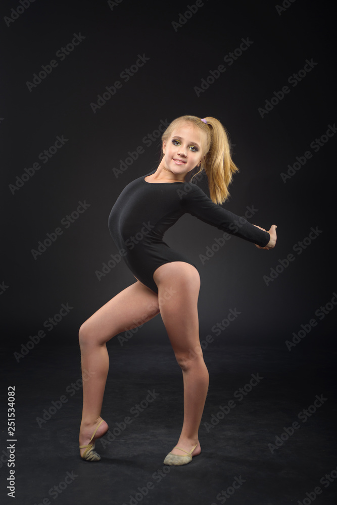 Young beautiful white caucasian girl gymnast with long hair doing gymnastic exercise on black background. Young beautiful white caucasian girl gymnast with long hair doing gymnastic exercise on black background.