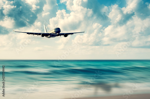 Airplane flying over blur tropical beach with smooth wave and sunset sky abstract background. © tonktiti