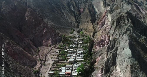 Aerial flying over Iruya, hidden town, at steep narrow valley surrounded of clouds, woods and dry colorful hills at background. Touristic town at Salta, Argentina