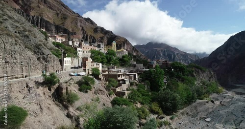 Aerial flying over Iruya, hidden town, at steep narrow valley surrounded of clouds, woods and dry colorful hills at background. Touristic town at Salta, Argentina