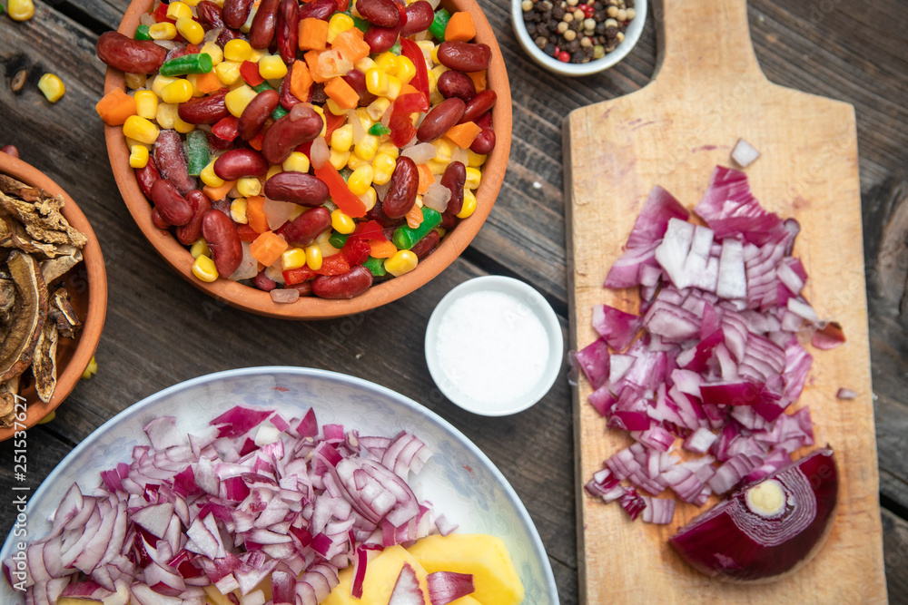 Mixture of vegetables, dried boletus mushrooms, sliced potato, red onion sliced and whole on a cutting board and spices, on old rustic wooden table. Mixture of vegetables, dried boletus mushrooms, sliced potato, red onion sliced and whole on a cutting board and spices, on old rustic wooden table.