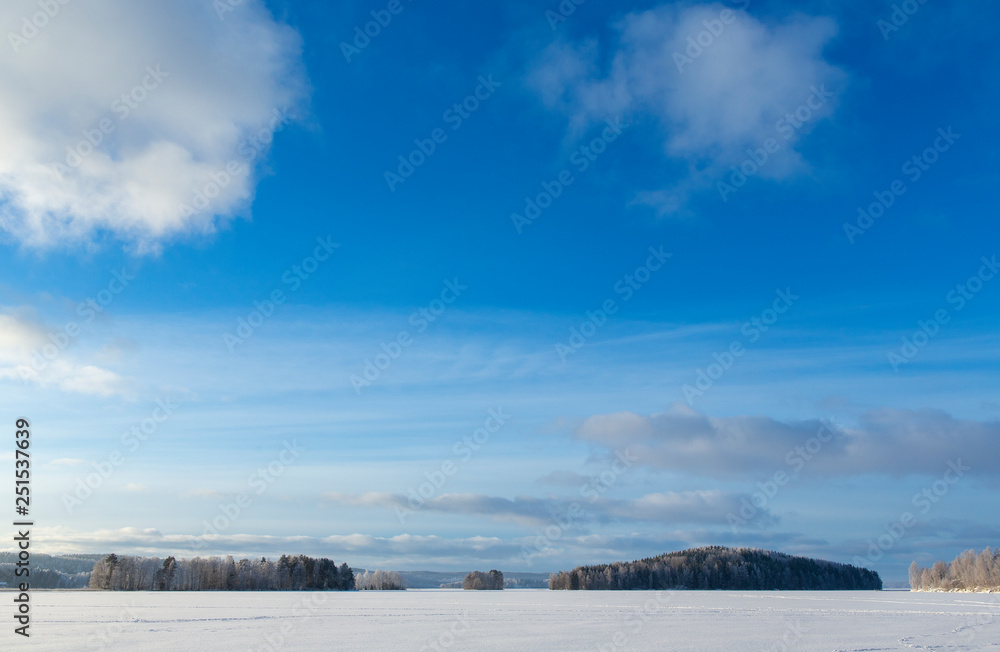 Obraz premium Winter wonderland view on the lake ice on a cold winter morning in Finland. Blue sky and sunrise in January.