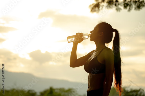 Sport asian girl drinking water from recycled plastic bottle in the mountains in the evening.