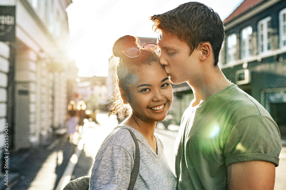 Young man kissing his smiling girlfriend on a city street - obrazy, fototapety, plakaty 
