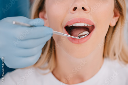 cropped view of dentist examining teeth of young woman with mouth mirror