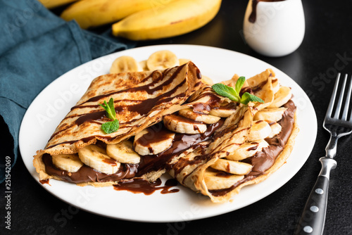 Tasty crepe with hazelnut chocolate spread and banana on white plate