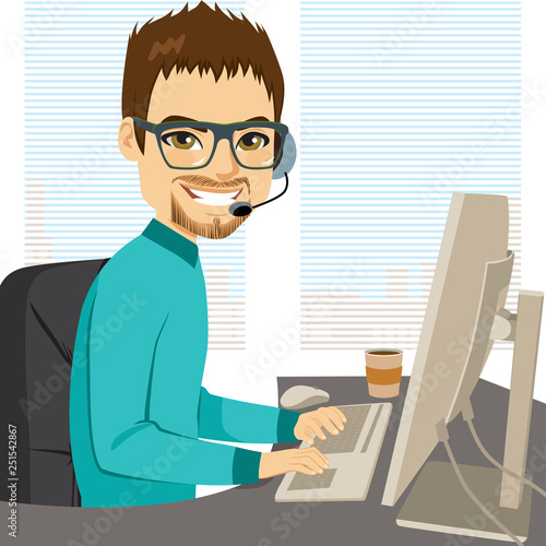 Young adult male help call center operator working on desk typing on computer keyboard and talking with headphones helpline concept