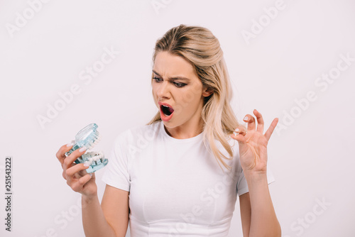 shocked woman in white t-shirt holding jaw model and tooth isolated on white