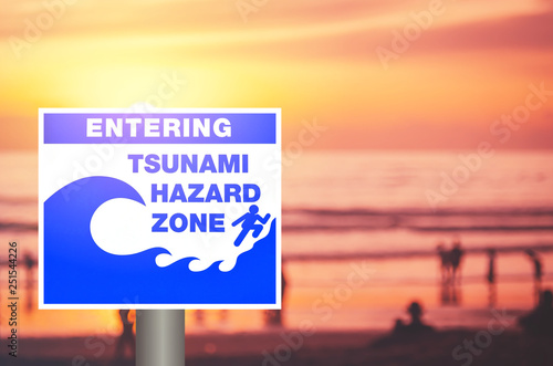 Tsunami warning sign on blur people relax on tropical sunset beach with bokeh sun light wave abstract background.