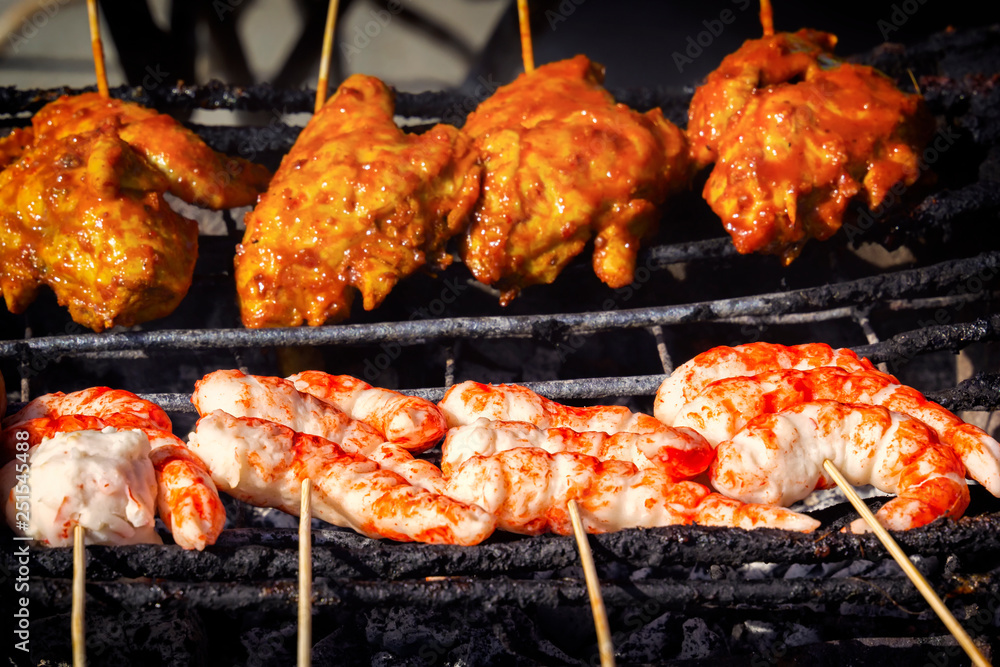 Traditional Asian food chicken wings, shrimps and sausages on wooden skewers - satay are grilled. Street food. Close-up