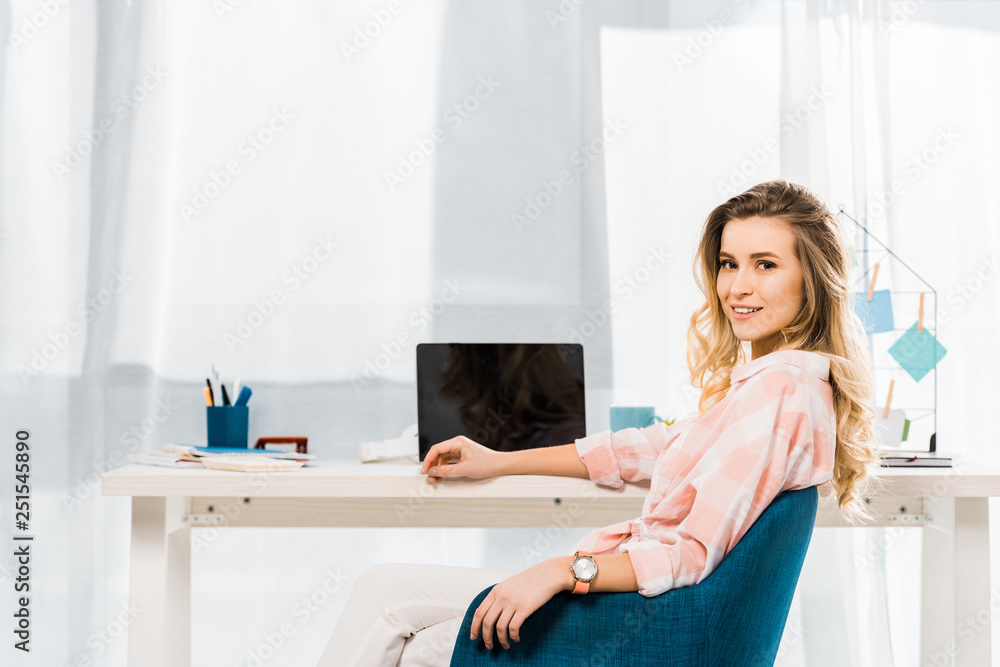 Attractive young woman in checkered shirt sitting at workplace and looking at camera Attractive young woman in checkered shirt sitting at workplace and looking at camera