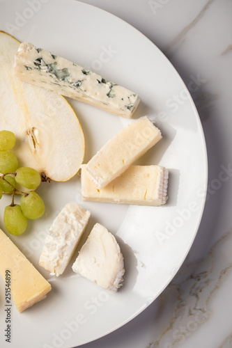 Käseteller mit Edamer, Parmesan, Blauschimmel Käse und Ziegenkäse an Birne und Trauben auf Teller und Marmor Hintergrund