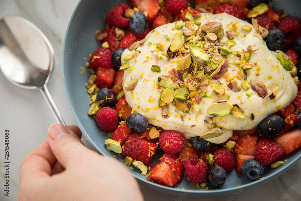 Frau isst Beeren Obstsalat mit Erdbeeren, Himbeeren, Blaubeeren, Pistazien, Zitronen Zesten, Leinöl Kurkuma Quark Creme in blauer Schale als Frühstück auf Marmor Hintergrund Frau isst Beeren Obstsalat mit Erdbeeren, Himbeeren, Blaubeeren, Pistazien, Zitronen Zesten, Leinöl Kurkuma Quark Creme in blauer Schale als Frühstück auf Marmor Hintergrund