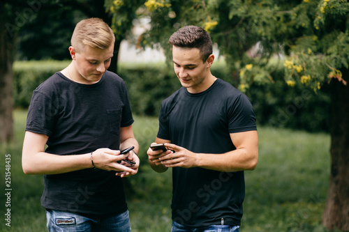 Two young men standing together outdoors looking at photos on a mobile phone