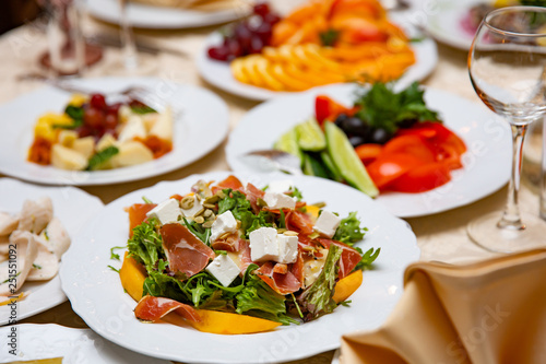 Fresh mix salad with ham, feta and mango on white plate. restaurant table setting