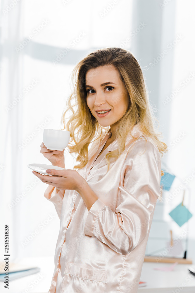 Pretty girl in satin pyjamas drinking coffee in morning and looking at camera Pretty girl in satin pyjamas drinking coffee in morning and looking at camera