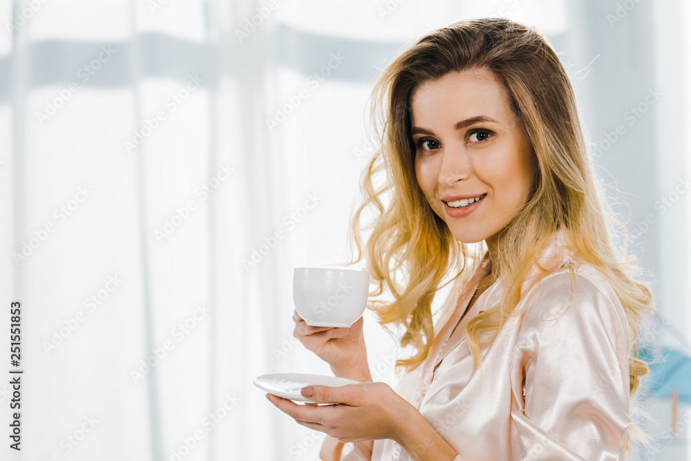 Blissful blonde woman in pyjamas drinking coffee in morning