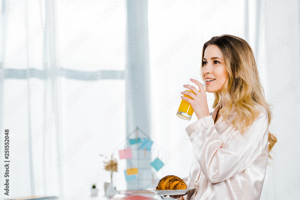 Inspired girl in pyjamas holding croissant and drinking orange juice in morning Inspired girl in pyjamas holding croissant and drinking orange juice in morning