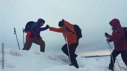 Climber helping teammate climb, the man with the backpack reached out a helping hand to his friend. Three climbers on a snow slope in the mountains, climbing to the top of the mountain in winter.