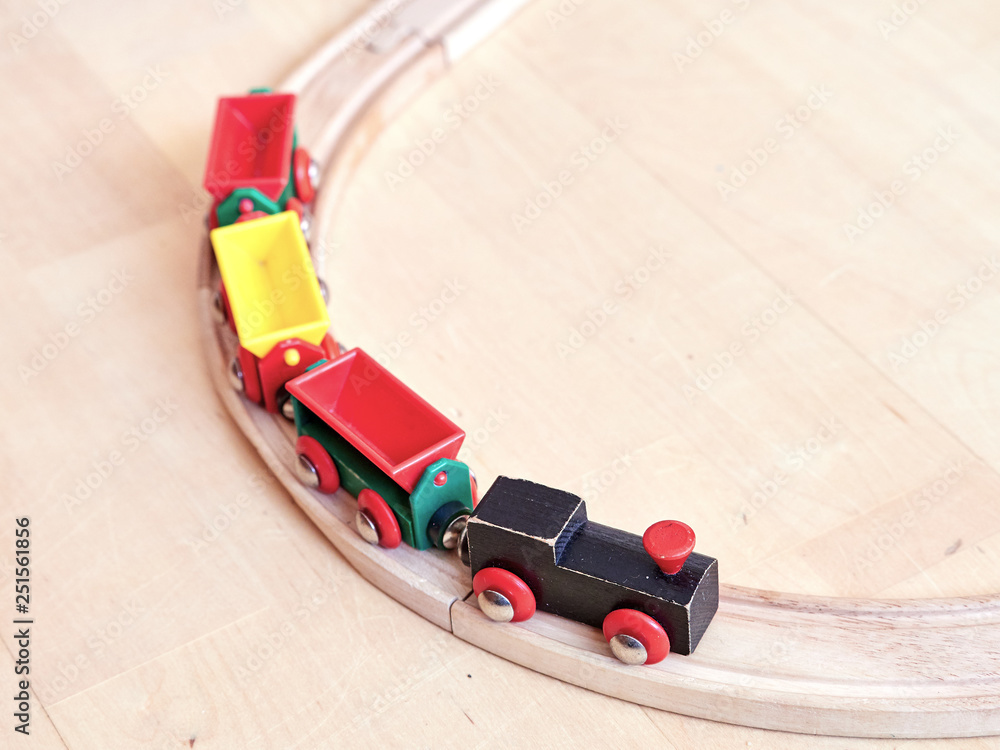Wooden toy train running on miniature railroad. The black engine pulling colorful cars on the floor. Educational toys for children in preschool and kindergarten.