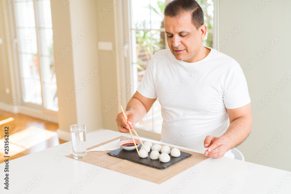 Middle age man eating asian dim sum using chopsticks at home Middle age man eating asian dim sum using chopsticks at home