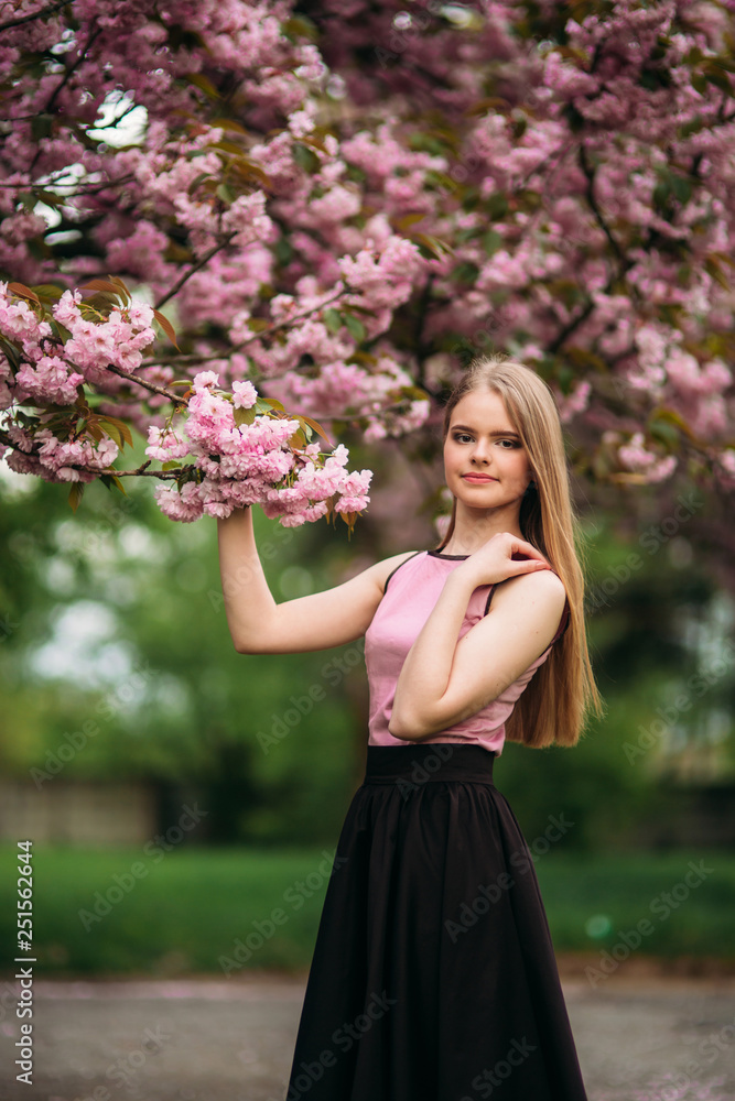 Portrait of European female near the Japanese flowering tree of sakura. Blond hair girl Portrait of European female near the Japanese flowering tree of sakura. Blond hair girl