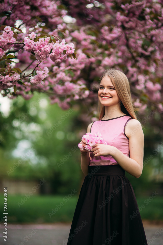Portrait of European female near the Japanese flowering tree of sakura. Blond hair girl Portrait of European female near the Japanese flowering tree of sakura. Blond hair girl