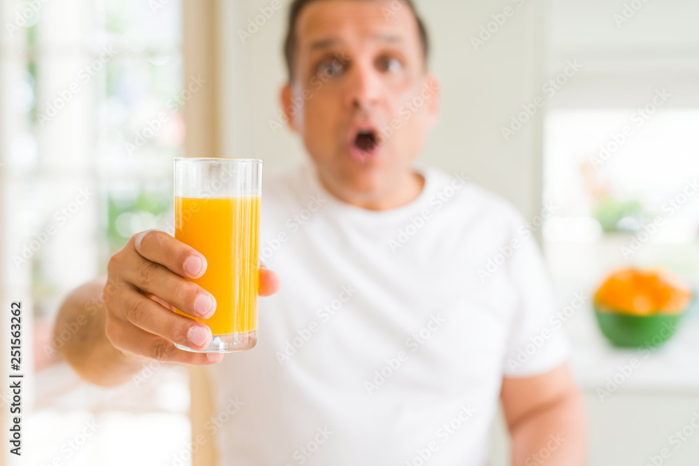 Middle age man drinking a glass of orange juice at home scared in shock with a surprise face, afraid and excited with fear expression Middle age man drinking a glass of orange juice at home scared in shock with a surprise face, afraid and excited with fear expression