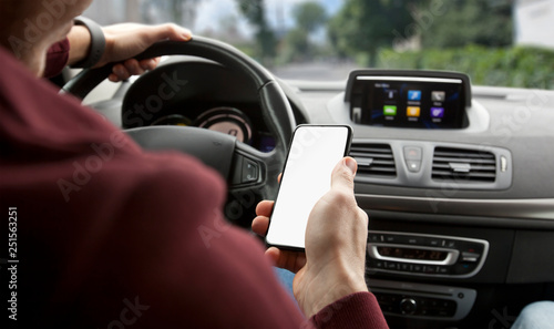 The young man holding mobile phone with white screen sitting in his car