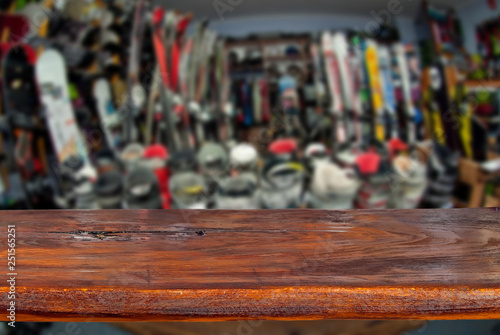 Mockup. Image of sport store with equipment for skiing. Defocused, blurred image. In the foreground is the top of a wooden table, counter. © Ivan