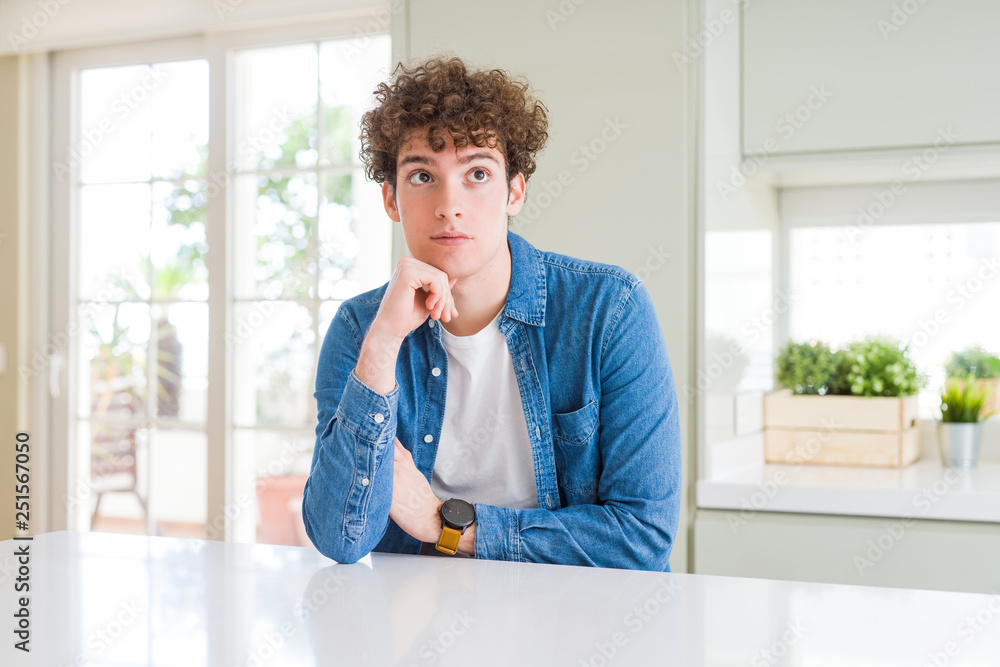 Young handsome man wearing casual denim jacket at home with hand on chin thinking about question, pensive expression. Smiling with thoughtful face. Doubt concept. Young handsome man wearing casual denim jacket at home with hand on chin thinking about question, pensive expression. Smiling with thoughtful face. Doubt concept.