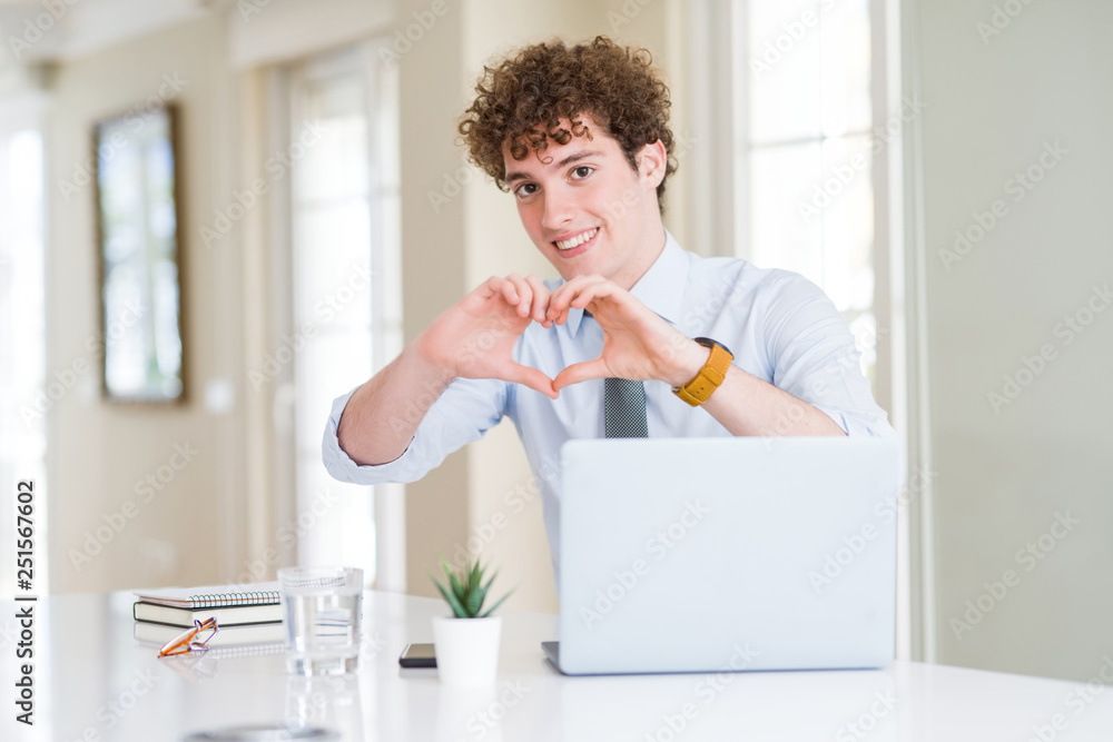 Young business man working with computer laptop at the office smiling in love showing heart symbol and shape with hands. Romantic concept.