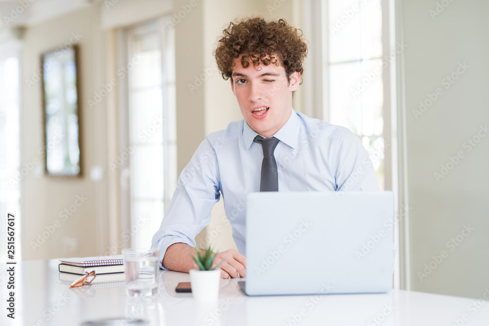 Young business man working with computer laptop at the office winking looking at the camera with sexy expression, cheerful and happy face. Young business man working with computer laptop at the office winking looking at the camera with sexy expression, cheerful and happy face.