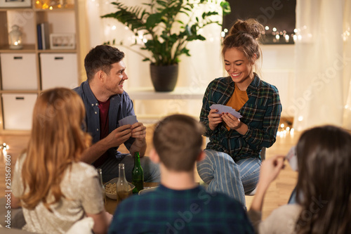 friendship, leisure and entertainment concept - happy friends with non-alcoholic beer playing cards game at home in evening