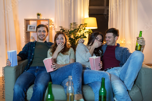 friendship and leisure concept - friends with non-alcoholic beer and popcorn watching tv at home in evening