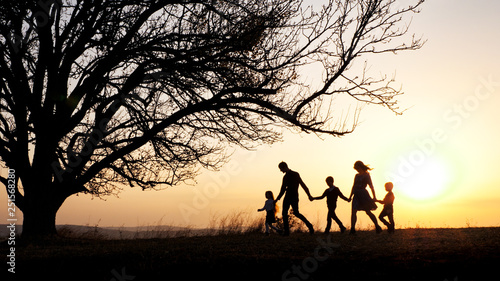 Silhouettes of happy family walking together in the meadow during sunset